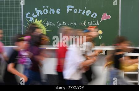 Stuttgart, Deutschland. Juli 2024. Am letzten Schultag vor den Sommerferien in Baden-Württemberg laufen Kinder der 4. Klasse einer Stuttgarter Grundschule an einer Tafel vorbei mit den Worten: 'Glückliche Ferien, alles Gute und viel Glück' (Wischeffekt durch lange Exposition). Quelle: Bernd Weißbrod/dpa/Alamy Live News Stockfoto