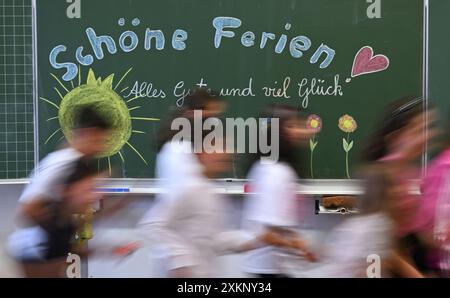 Stuttgart, Deutschland. Juli 2024. Am letzten Schultag vor den Sommerferien in Baden-Württemberg laufen Kinder der 4. Klasse einer Stuttgarter Grundschule an einer Tafel vorbei mit den Worten: 'Glückliche Ferien, alles Gute und viel Glück' (Wischeffekt durch lange Exposition). Quelle: Bernd Weißbrod/dpa/Alamy Live News Stockfoto