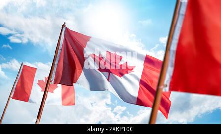 Eine kanadische Flagge fliegt an einem sonnigen Tag am Himmel. Die Flagge ist rot und weiß mit einem Ahornblatt. Der Himmel ist blau mit ein paar Wolken und die Sonne Stockfoto