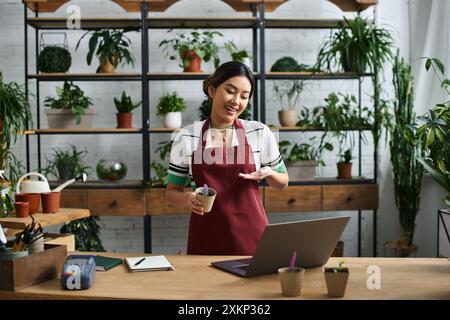 Eine junge asiatische Frau, die Besitzerin eines kleinen Pflanzenladens, lächelt, während sie ihren Kunden neue Pflanzen vorstellt. Stockfoto