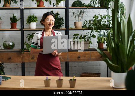 Eine glückliche Asiatin in einer Schürze arbeitet an ihrem Laptop in ihrem Fabrikladen. Stockfoto