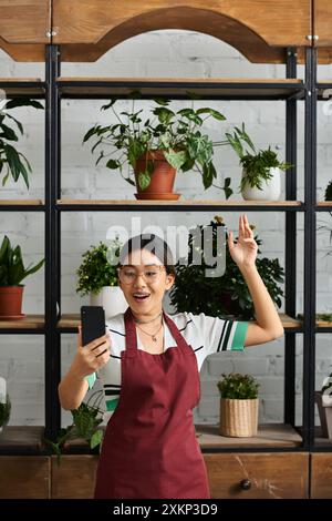 Eine Asiatin, die Eigentümerin eines Pflanzenladens, begrüßt ihre Kunden mit einem Lächeln und einer Welle. Stockfoto