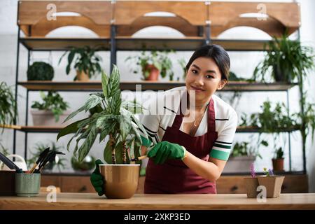 Eine lächelnde asiatische Frau auf einer Schürze arbeitet in ihrem Pflanzenladen und pflegt eine lebendige grüne Pflanze. Stockfoto