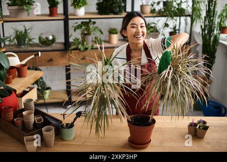 Eine lächelnde Asiatin in einer Schürze pflegt Pflanzen in ihrem Laden. Stockfoto