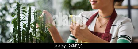 Eine junge Frau in einer Schürze sprüht sanft Wasser auf eine Pflanze in ihrem kleinen Pflanzenladen. Stockfoto