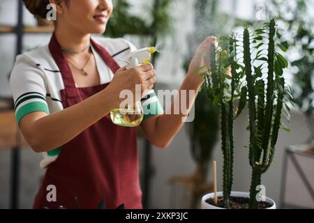 Eine junge asiatische Frau mit roter Schürze bewässert sanft eine Pflanze in ihrem Pflanzenladen. Stockfoto