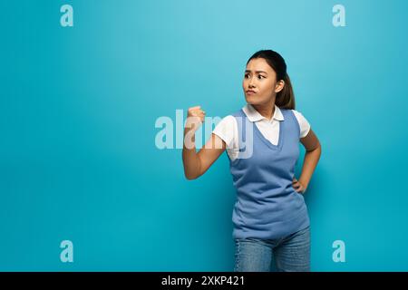 Eine junge asiatische Frau in eleganter Freizeitkleidung steht selbstbewusst vor blauem Hintergrund. Stockfoto