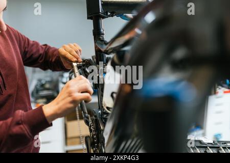 Nahaufnahme der Hände eines Mechanikers mit einem Ratschenschlüssel, um am Rahmen und an der Hinterradaufhängung eines E-Mountainbikes zu arbeiten. Stockfoto