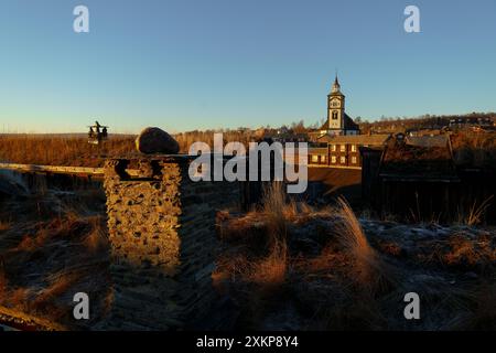 Sonnenuntergänge beleuchten die bezaubernde Landschaft von Roros, mit der Wahrzeichen der Stadt Kirche und Holzarchitektur Stockfoto