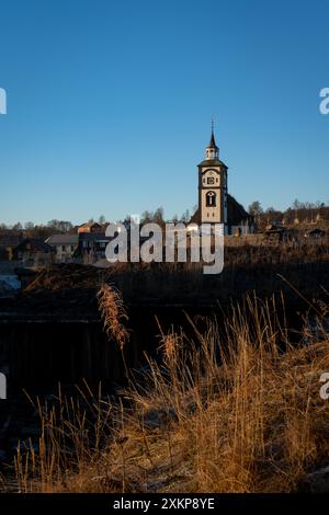 Sonnenuntergänge beleuchten die bezaubernde Landschaft von Roros, mit der Wahrzeichen der Stadt Kirche und Holzarchitektur Stockfoto