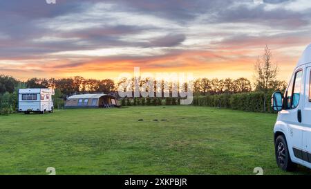 Panoramalandschaft mit wunderschönem Sonnenuntergang auf einem Bauerncamping mit Familienzelten und einem alten Wohnmobil in Drenthe, Niederlande Stockfoto