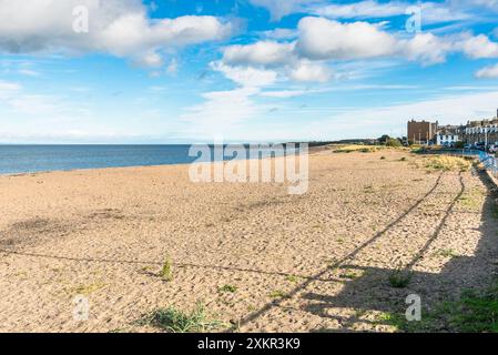 Großer Sandstrand gesäumt von alten Reihenhäusern an einem sonnigen Herbsttag. Menschen, die am Strand entlang schlendern, sind in der Nähe zu sehen. Stockfoto