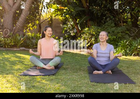 Yoga im Freien üben, asiatische Großmutter und Enkelin meditieren auf Yogamatten im Garten Stockfoto