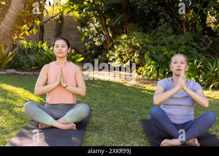 Yoga im Freien üben, asiatische Großmutter und Enkelin meditieren auf Yogamatten im Garten Stockfoto