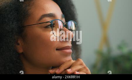 Schließen Sie die afroamerikanische Geschäftsfrau mit Brille, die wegschaut und denkt, lächelnd nachdenklich, nachdenkliches ethnisches Mädchen, glückliche, fröhliche Geschäftsfrau in Brille Stockfoto