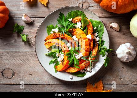 Herbstsalat mit gegrilltem Kürbis, Fetakäse und Kräutern auf Holztisch, Kopierraum, Draufsicht. Warmes Salatrezept im Herbst der Saison, vegetarischer Komfort Stockfoto