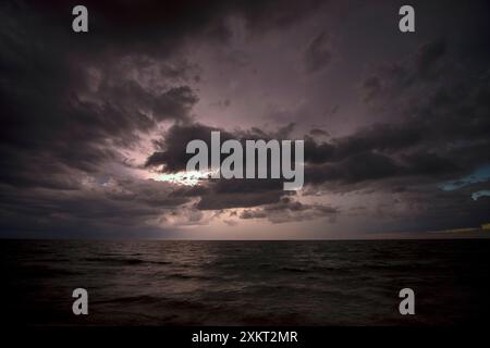 Gewitterwolken über rauem Meereswasser. Abendliche Meereswellen brechen am Sandstrand. Wunderschöne Meereslandschaft bei Sonnenuntergang Stockfoto