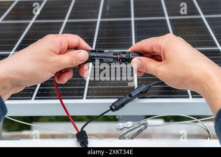 Nahaufnahme der Hände des Technikers, die mc4-Steckverbinder über dem Solarpanel verbinden. Erneuerbare Energien und Nachhaltigkeitskonzept Stockfoto