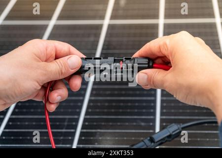 Nahaufnahme der Hände des Technikers, die mc4-Steckverbinder über dem Solarpanel verbinden. Erneuerbare Energien und Nachhaltigkeitskonzept Stockfoto