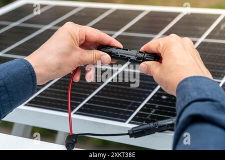 Nahaufnahme der Hände des Technikers, die mc4-Steckverbinder über dem Solarpanel verbinden. Erneuerbare Energien und Nachhaltigkeitskonzept Stockfoto