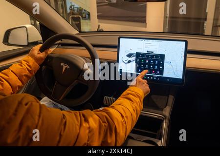 Nahaufnahme männlicher Hände verwendet Display, greifen Lenkrad Tesla Modell Y Elektroauto während der Probefahrt, Prozesstest und Bewertung von Autos durch Potenti Stockfoto