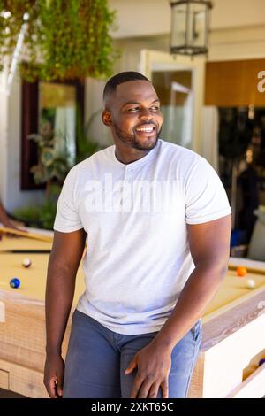 Lächelnder afroamerikanischer Mann, der sich auf den Billardtisch lehnt und die Freizeit zu Hause genießt Stockfoto