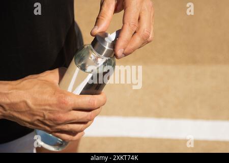 Glasflasche Wasser in Sportmannhänden auf dem Sportplatz im Freien. Konzept Wasserhaushalt für die heiße Jahreszeit zum Workout. Nahaufnahme. Kopierbereich. Stockfoto