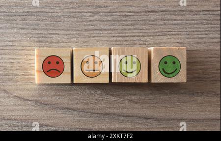 Stimmungseinschätzung mit Emoticons auf Holzwürfeln auf einem Holztisch. Draufsicht. Stockfoto