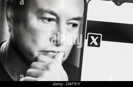 Elon Musk schaut sich ein Smartphone mit dem neuen Twitter-Logo an. Speicherplatz auf Ihrem Smartphone kopieren. Stockfoto