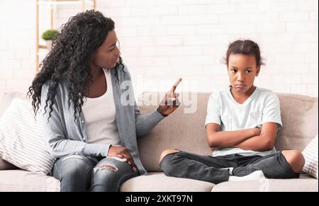 Das Konzept Der Familiendisziplin. Mürrische schwarze Mutter schimpfte ihre freche kleine Tochter zu Hause auf dem Sofa Stockfoto