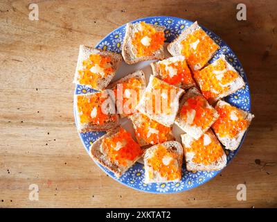 Teller mit Brotscheiben mit Lachseiern und Butter Eine hölzerne Oberfläche Stockfoto