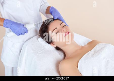 Der Kosmetiker macht die Mikrostromtherapie gegen Haarausfall am Haar in einem Schönheitssalon. Kosmetologie und professionelle Hautpflege. Stockfoto