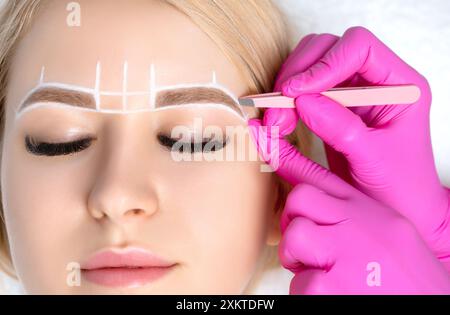 Frau mit Permanent Make-up Tattoo auf den Augenbrauen. Wimperntusche zupft die Augenbrauen mit einer Pinzette. Professionelle Make-up- und Kosmetikpflege. Stockfoto
