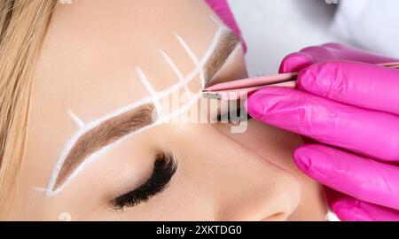 Frau mit Permanent Make-up Tattoo auf den Augenbrauen. Wimperntusche zupft die Augenbrauen mit einer Pinzette. Professionelle Make-up- und Kosmetikpflege. Stockfoto