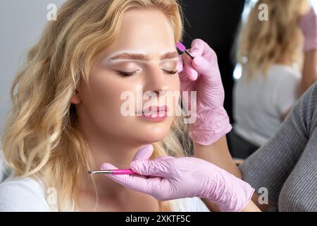 Blonde Frau mit permanentem Make-up Tattoo auf den Augenbrauen. Nahaufnahme-Kosmetikerin, die Augenbrauen tätowiert. Professionelle Make-up- und Kosmetikpflege Stockfoto