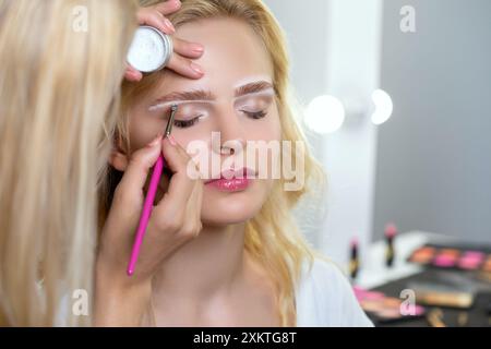 Blonde Frau mit permanentem Make-up Tattoo auf den Augenbrauen. Nahaufnahme-Kosmetikerin, die Augenbrauen tätowiert. Professionelle Make-up- und Kosmetikpflege Stockfoto