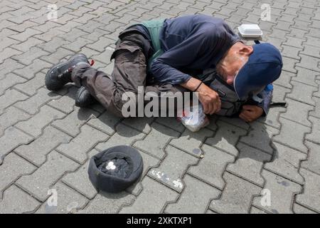 Ein betäubender Mann, der für Geld auf der Straße liegt, ein armer, obdachloser Obdachloser in der Hocke Stockfoto