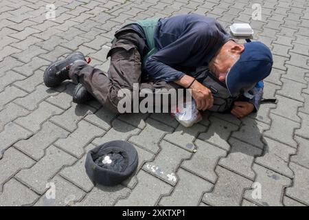 Ein betäubender Mann, der wegen Geld auf der Straße liegt, ein armer Vagabond, obdachlos gehockt Stockfoto