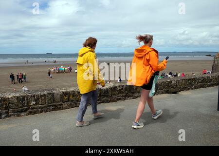 Frauen in Regenmänteln gehen entlang des Küstenweges in Broad Haven Blick auf die Menschen am Strand im Sommer Pembrokeshire Wales Großbritannien Juni 2024 KATHY DEWITT Stockfoto