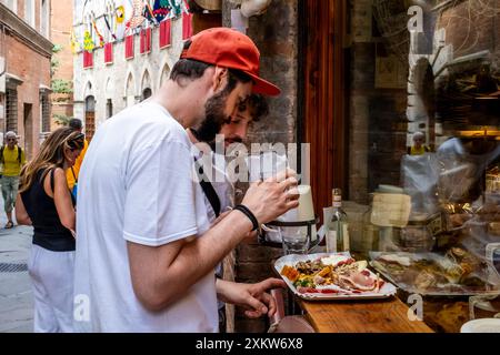 Zwei junge Männer genießen ein Mittagessen vor Einem Delikatessengeschäft in Siena, Toskana, Italien. Stockfoto
