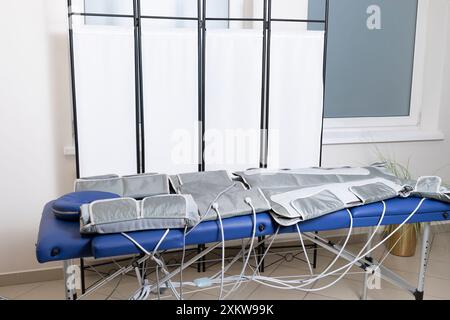 pressotherapie grauer Massageanzug auf blauem Sofa im Spa, Behandlung von Krampfadern, Ödemen, Lymphdrainage, Gewichtsverlust. Leere Pressotherapie Stockfoto