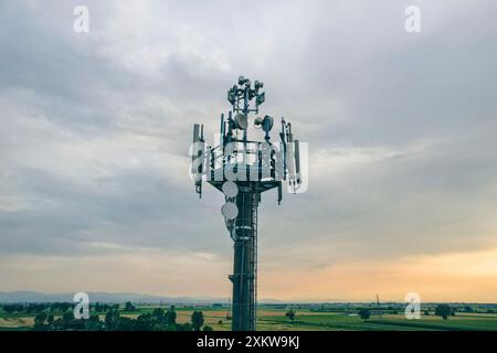 Antenne, Telekommunikationsturm mit Antennen über blauem Himmel und weißen Wolken, die bei Sonnenuntergang Daten auf dem Land übertragen. Drohnenansicht, pov Stockfoto