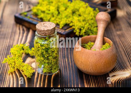 Ein Holzmörtel und Pistill sitzt auf einem Holztisch, gefüllt mit getrockneten gelben Blumen. Neben dem Mörtel befindet sich ein Glasgefäß mit einem Korkdeckel, der auch d enthält Stockfoto