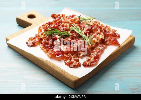 Scheiben von leckerem gebratenem Speck und Rosmarin auf hellblauem Holztisch Stockfoto