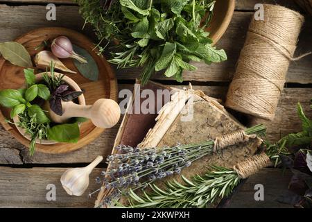 Verschiedene aromatische Kräuter, Mörtel mit Stößel, Garn und Gewürze auf Holztisch, flach gelegt Stockfoto