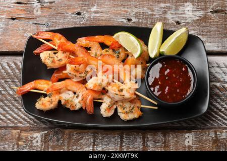 Köstliche gegrillte Garnelenspieße mit Sauce und Limette auf Holztisch, Blick von oben Stockfoto