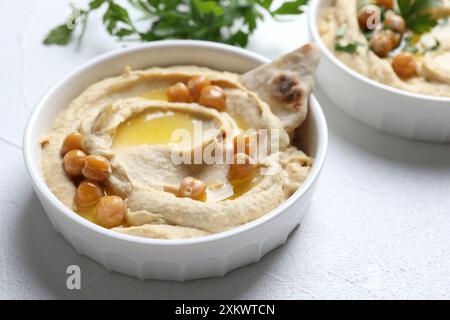 Köstlicher Hummus mit Olivenöl, Kichererbsen und Pita in einer Schüssel auf einem hellen, strukturierten Tisch Stockfoto