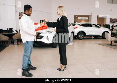 Porträt einer blonden Verkäuferin im Business-Anzug, die den Kunden die Hand schüttelt, redet, Autoschlüssel gibt. Stilvolle Autohändlerin, die Kunden bedient Stockfoto