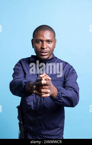 afroamerikanischer Bodyguard, der eine imaginäre Waffe auf die Kamera zeigt, ahmt Schießübungen nach. Porträt eines selbstbewussten Sicherheitsagenten hält seine Hand in Form einer Waffenpistole. Stockfoto