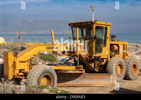 Caterpillar Straßengrader auf einer Baustelle in Kapstadt mit Tafelberg und dem Ozean im Hintergrund. Stockfoto